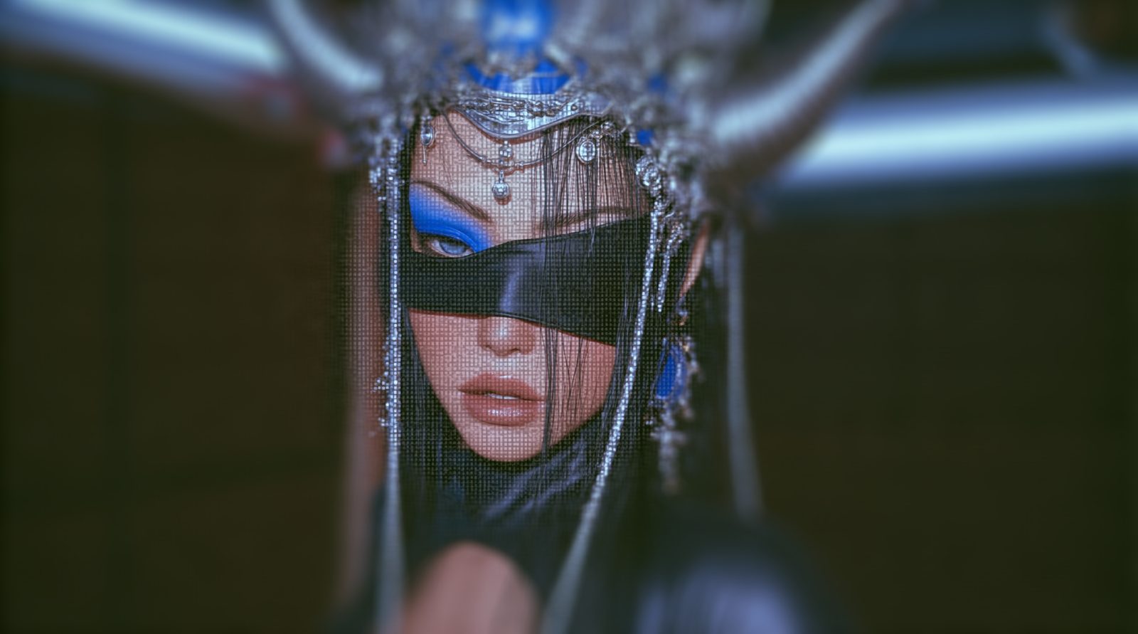 Portrait of a figure in an ornate silver and sapphire headdress, a black band drawn across her face, seen through a fine screen